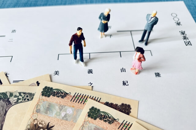 家系図の上に人形と紙幣が置かれ、相続した家をめぐる話し合いを表している